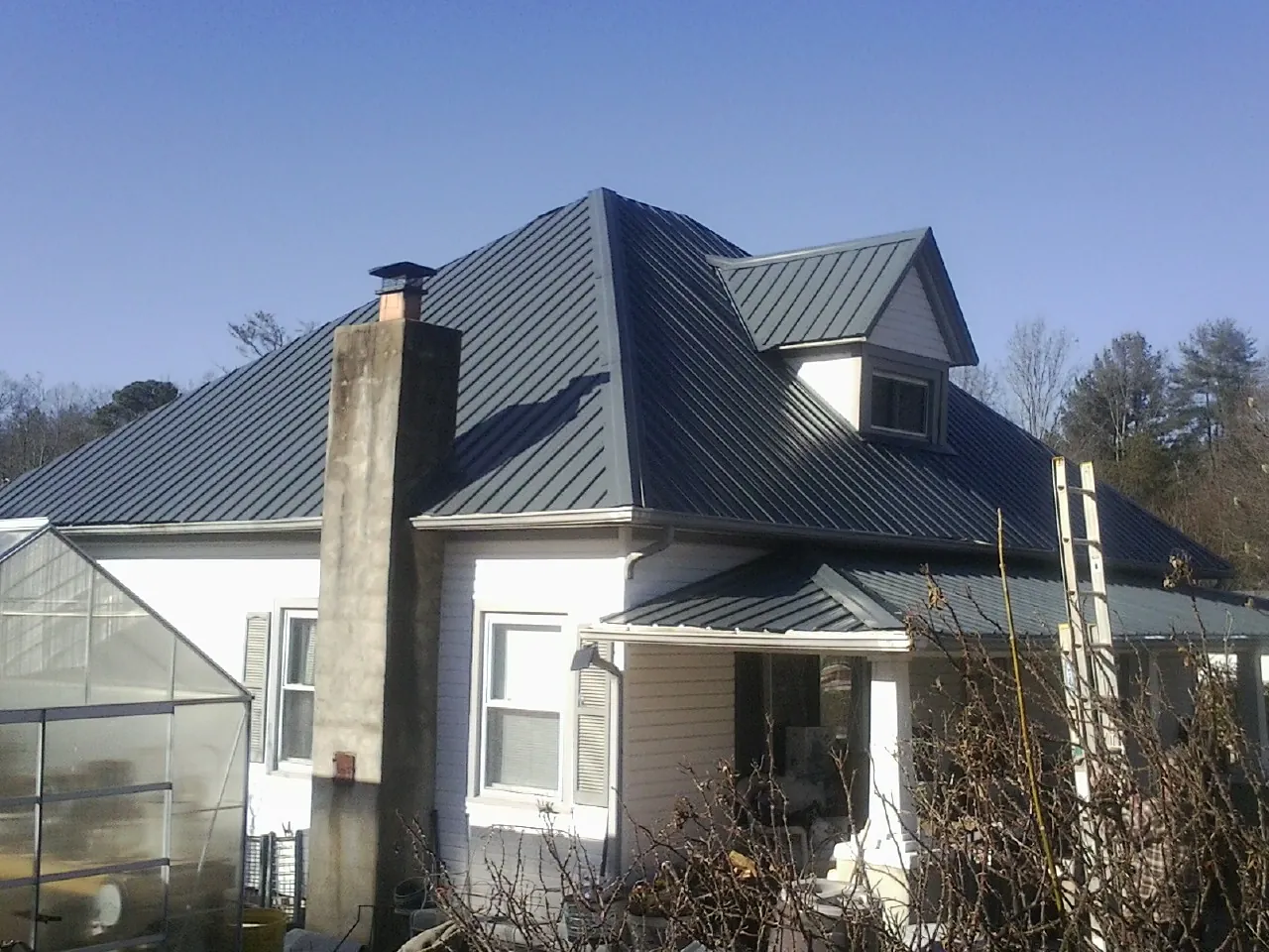 Dark blue standing seam metal roof on a white farmhouse with dormer — Slate & Tile Roof Repair by Roofing Brothers in Twin Mountain