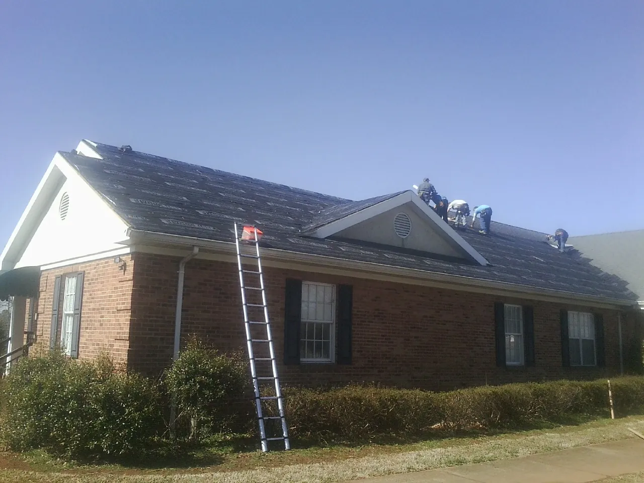 Crew tearing shingles off a brick ranch roof with a ladder set — Emergency Roof Repair work by our crew in Twin Mountain