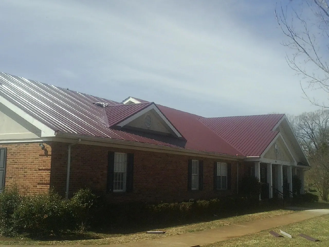 Red metal roof with gabled entries on a long brick building, from a Hail Damage Roof Repair job in Twin Mountain