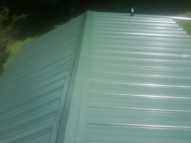New green metal panels meeting at the ridge of a roof — Flat Roof Repair work by our crew in Twin Mountain