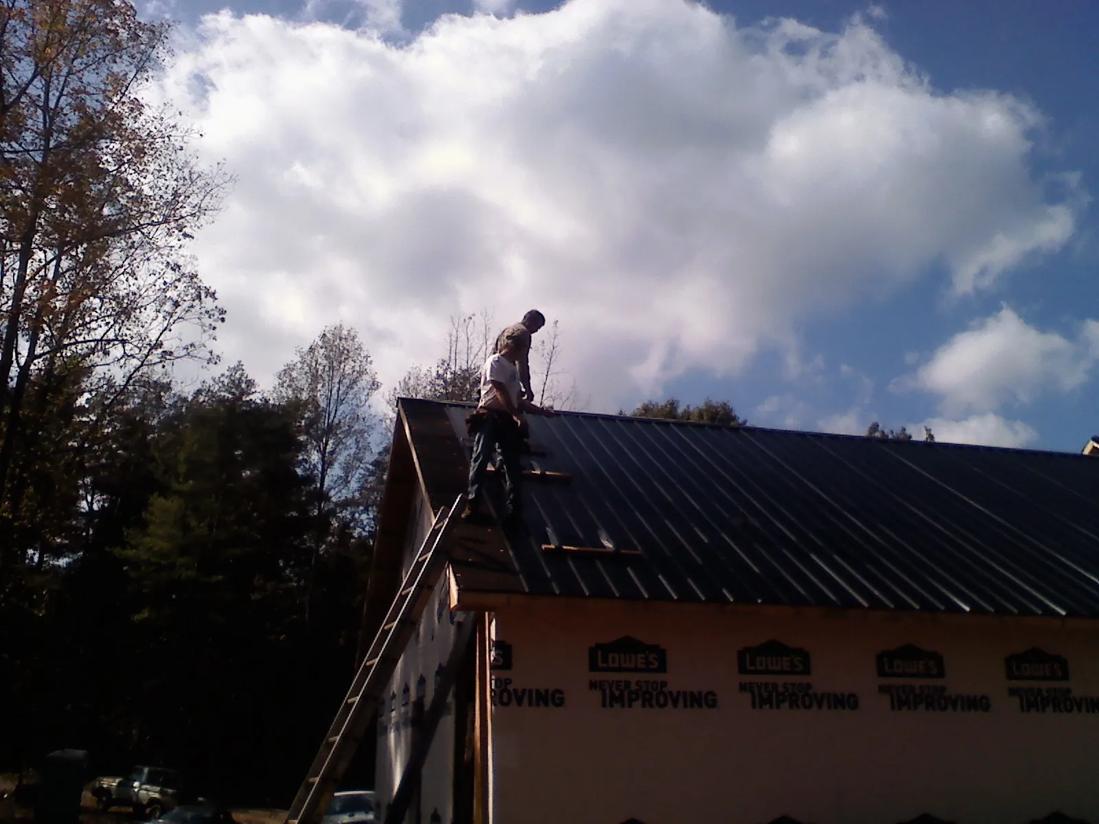 Roofer fastening dark metal panels high against a cloudy sky, from a Roof Inspection job in Twin Mountain
