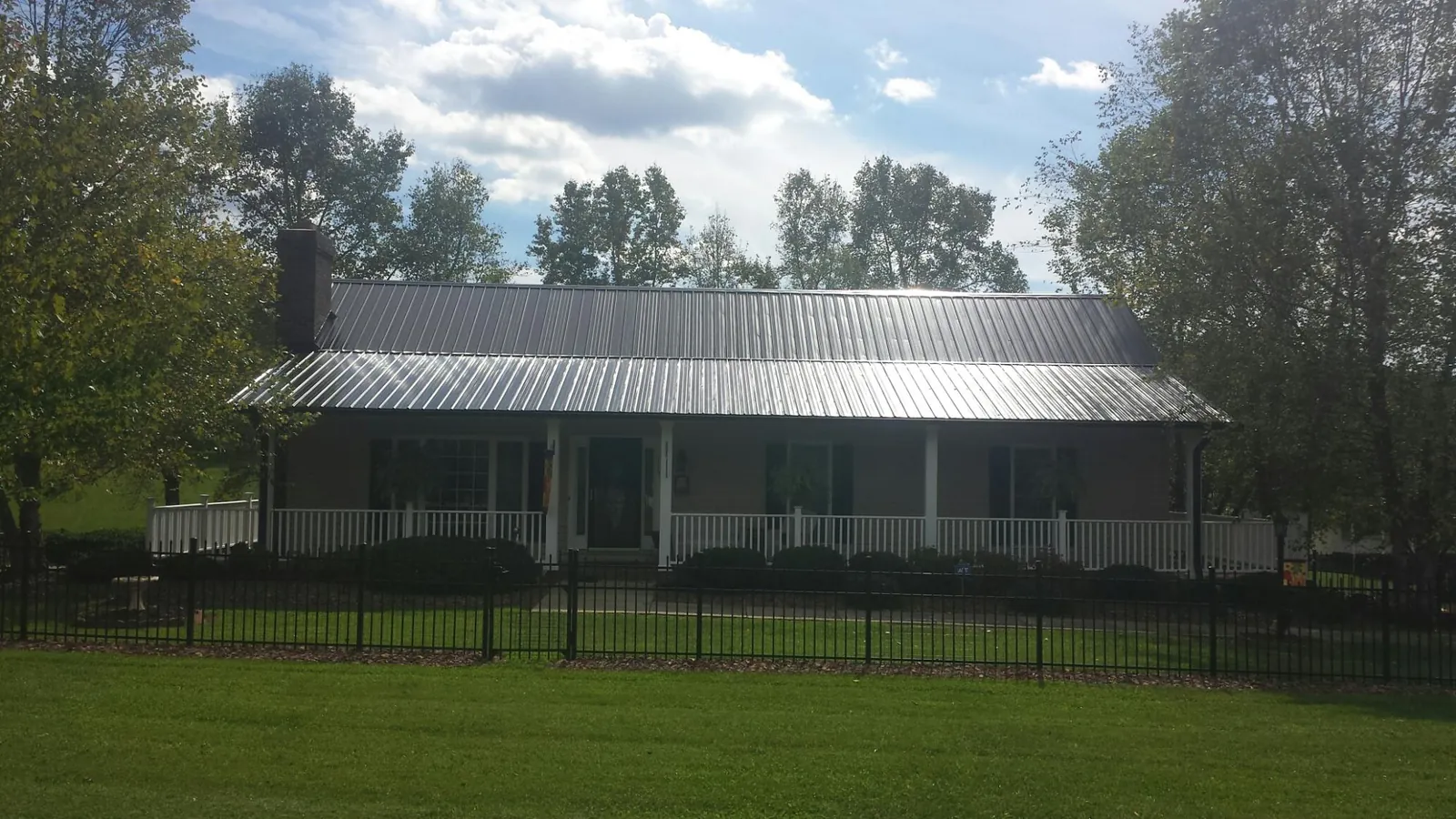Gray metal roof on a brick ranch with a full width front porch — Gutter Guard Installation work by our crew in Twin Mountain