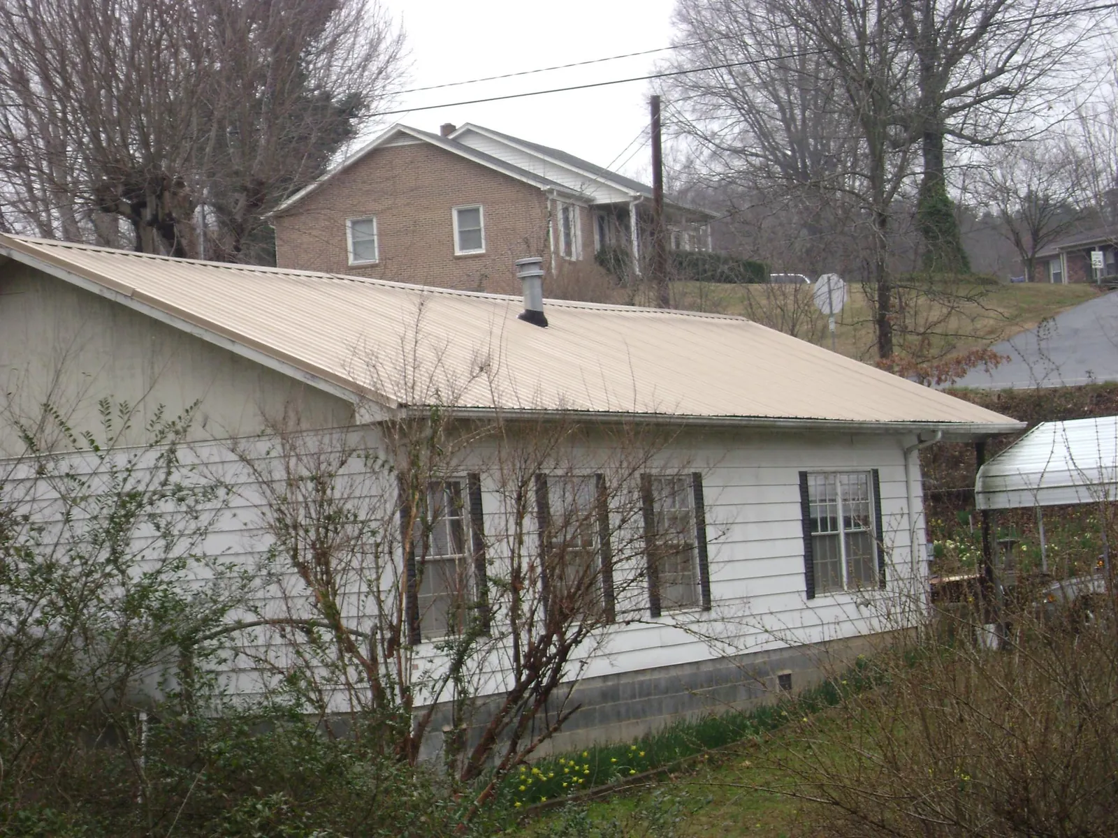 Tan metal roof on a white sided house set into a hillside — Commercial Roofing by Roofing Brothers in Twin Mountain