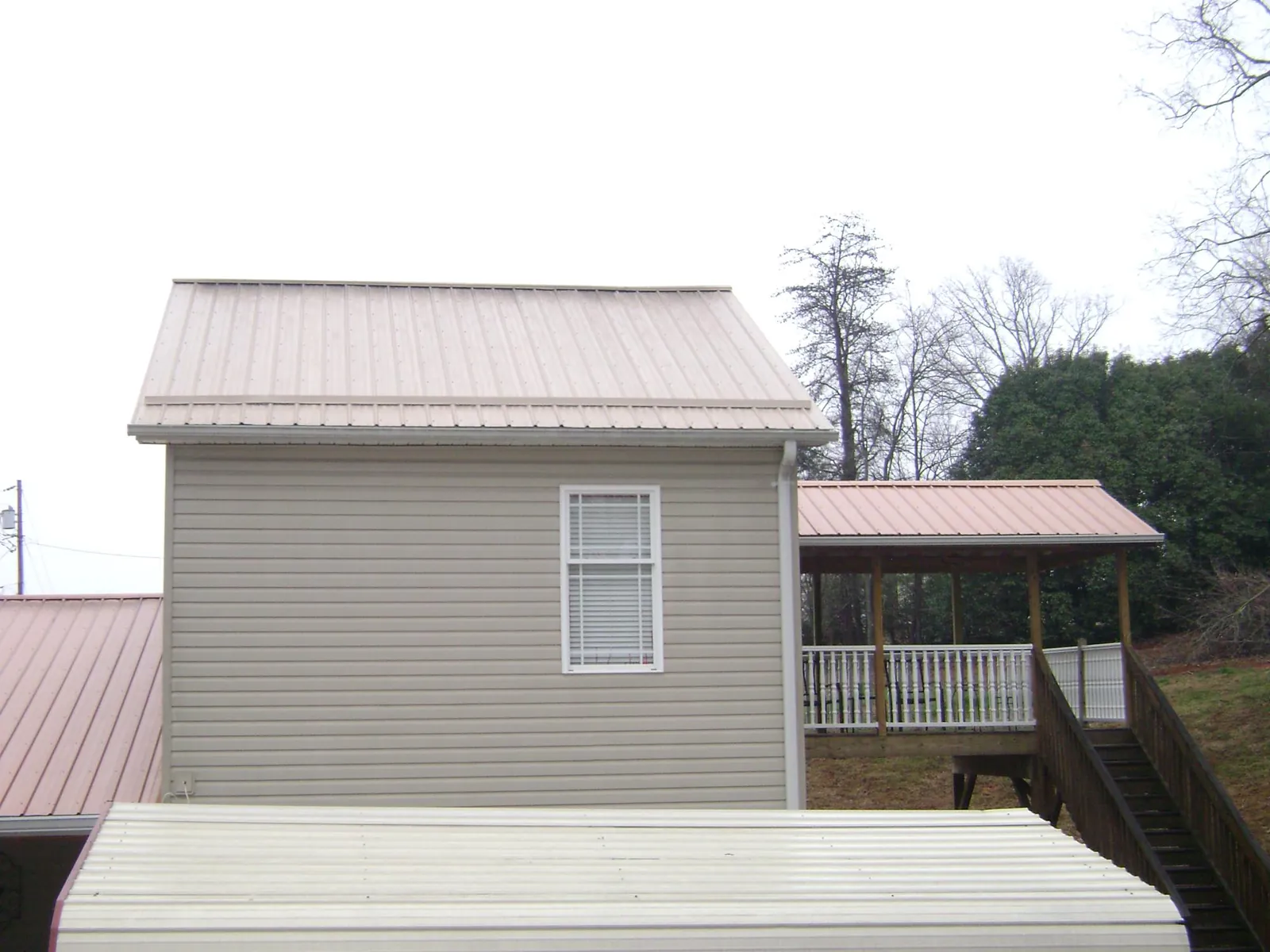 Tan metal roofs on a two story addition and attached porch, from a Roof Replacement job in Twin Mountain